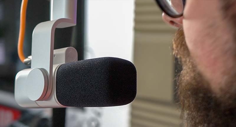 Image shows part of the face of a man, speaking in to the Logitech Blue Sona mic. The man is in a sound booth with sound insulation on the walls.