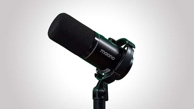 Image shows a black Maono PD200x microphone, fixed on the end of a desk stand and pointing upwards to the top left corner of the frame.
