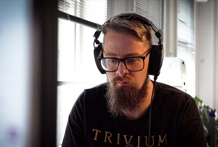 A man wearing the RØDE NTH100 headphones, sitting in an office and looking down at a screen.
