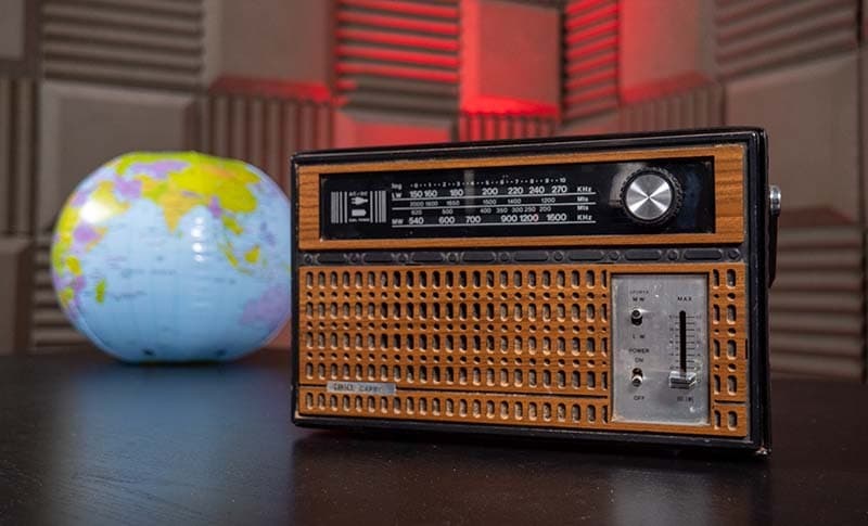 An old brown 1960s radio set on a table, with an inflatable globe behind it.
