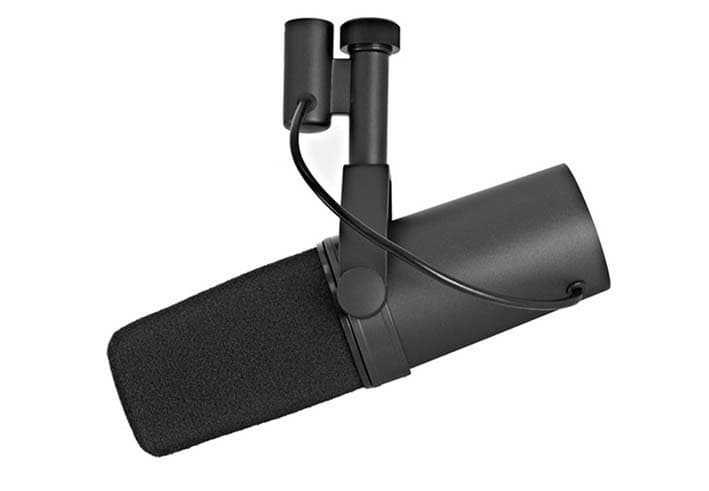 Image shows a SHURE SM7B microphone hanging from a mic stand, against a white background. The SM7B is a black caapsule microphone, and the black muff covers just less than half of the whole microphone.