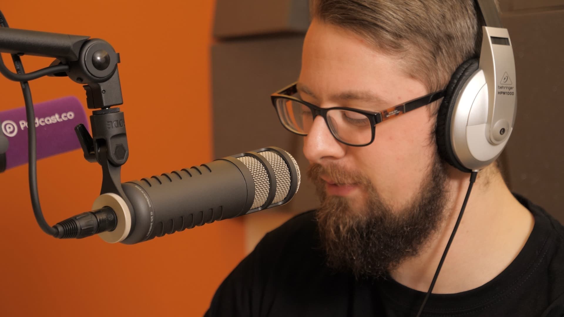 A man wearing headphones talking in to the Rode Procaster microphone whilst looking down.
